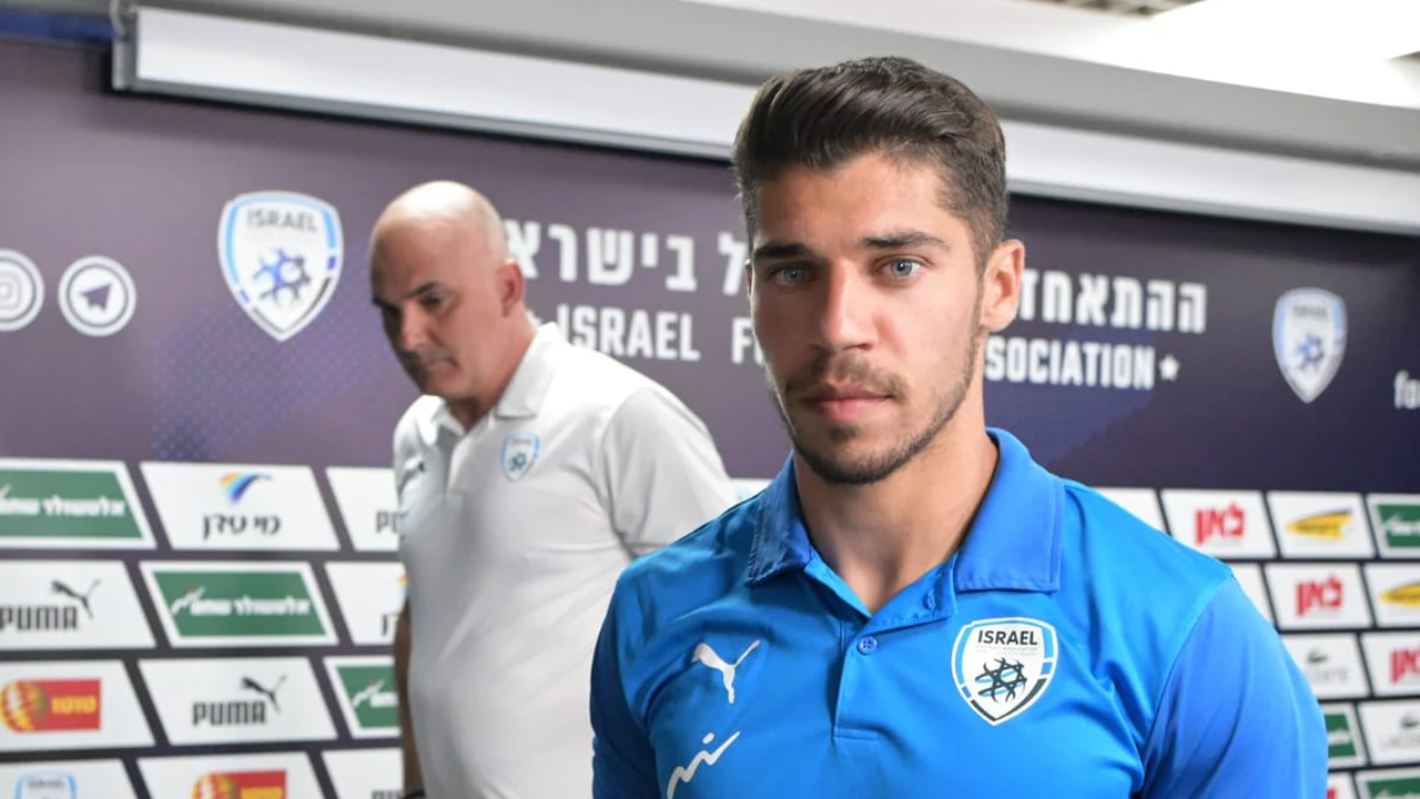 Footballer facing reporters at a press conference in front of a sponsor wall